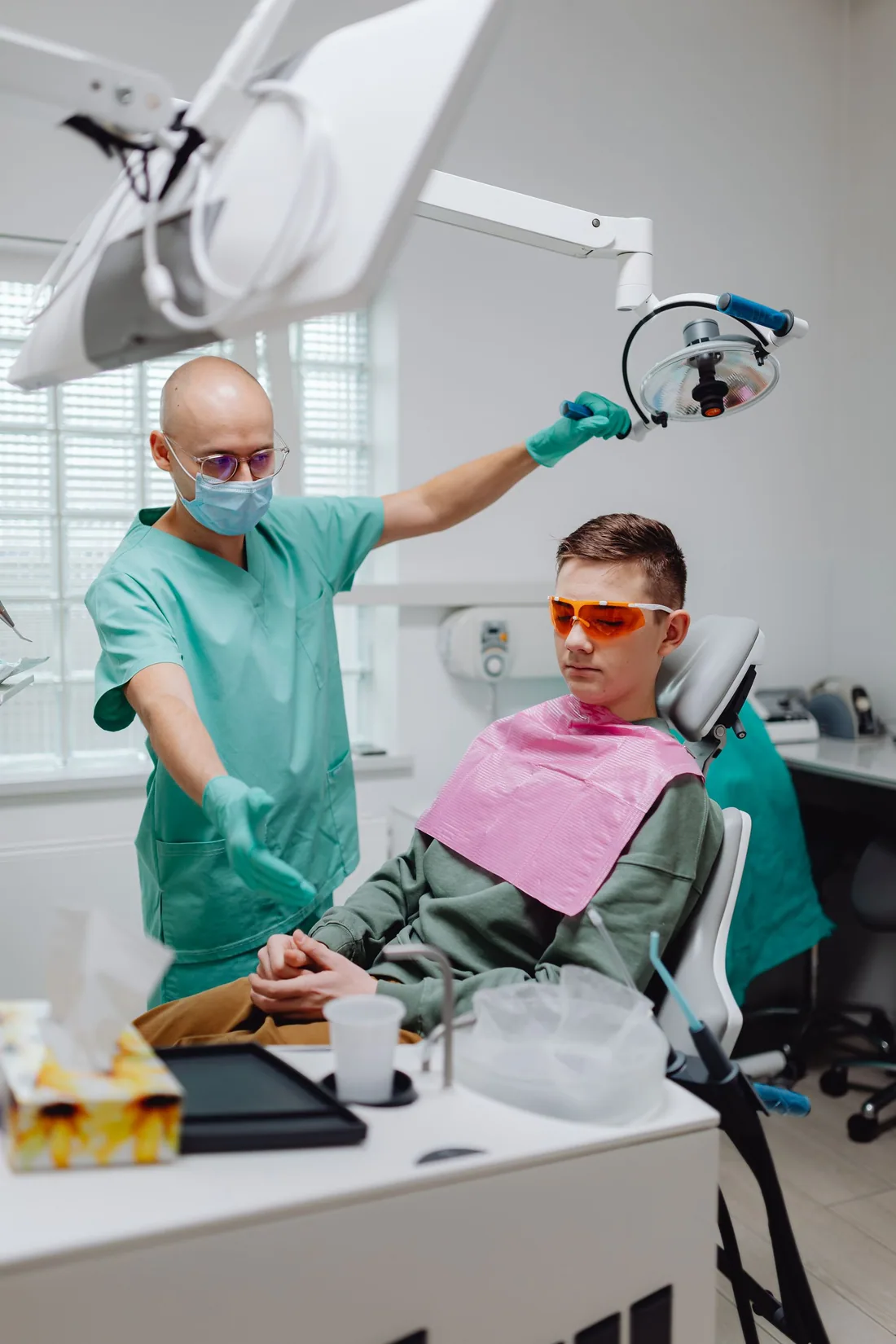 A dental professional prepares the light for a young patient in a treatment room