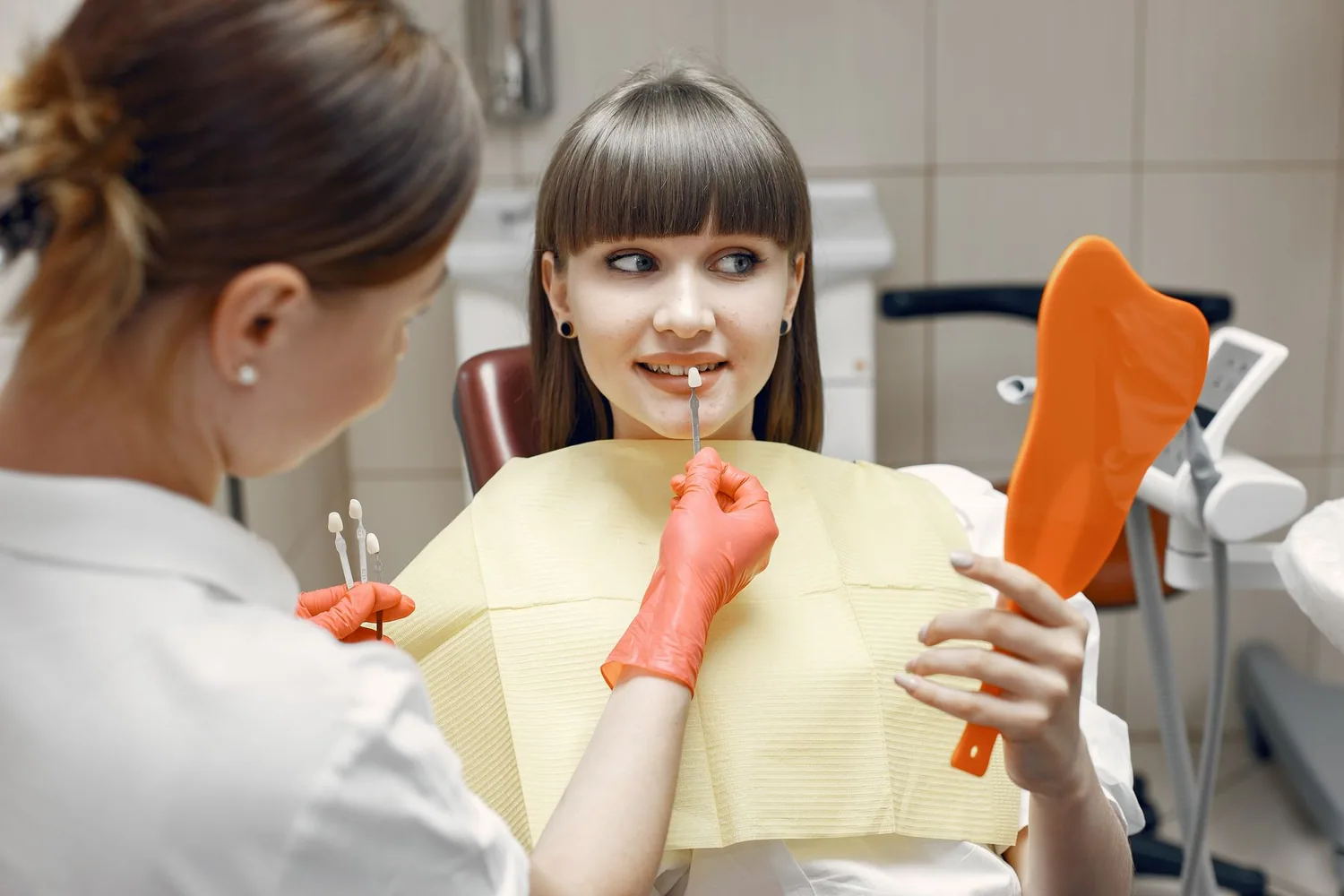 A patient compares a tooth shade with a dental professional in a treatment room